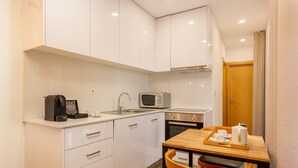 Una cocina pequeña con armarios blancos, microondas, cafetera y una mesa de madera con sillas.