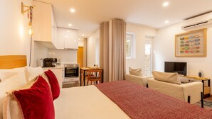 Una habitación de hotel con cama, escritorio, silla, televisor y kitchenette.