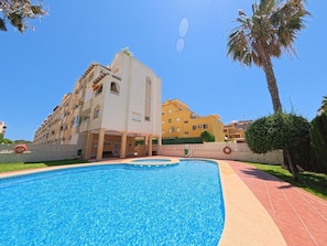 A swimming pool with a clear blue water surface, surrounded by a paved walkway.