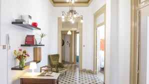 A hallway with a checkered floor, a chandelier, a green armchair, and a desk with a lamp and books. - Large bright apartment in Liberty building - Excellent position (Palermo)