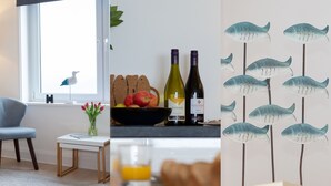 A room with a window, a table with a vase of tulips, a bowl of fruit, and two bottles of wine.