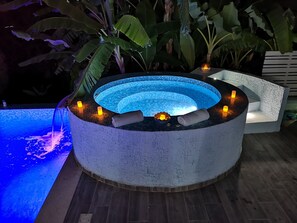 Een rond hottub met een geribbelde buitenkant, omringd door planten en kaarsen.