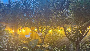 Een houten terras omringd door weelderige begroeiing en een hek met lichtjes.