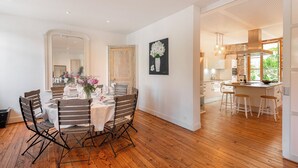Een eetgedeelte met een houten tafel en stoelen, een spiegel en een bloemen schilderij aan de muur.