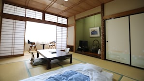 Une pièce traditionnelle japonaise avec un sol recouvert de tatamis, une table basse, un lit avec une couverture bleue et des portes coulissantes.