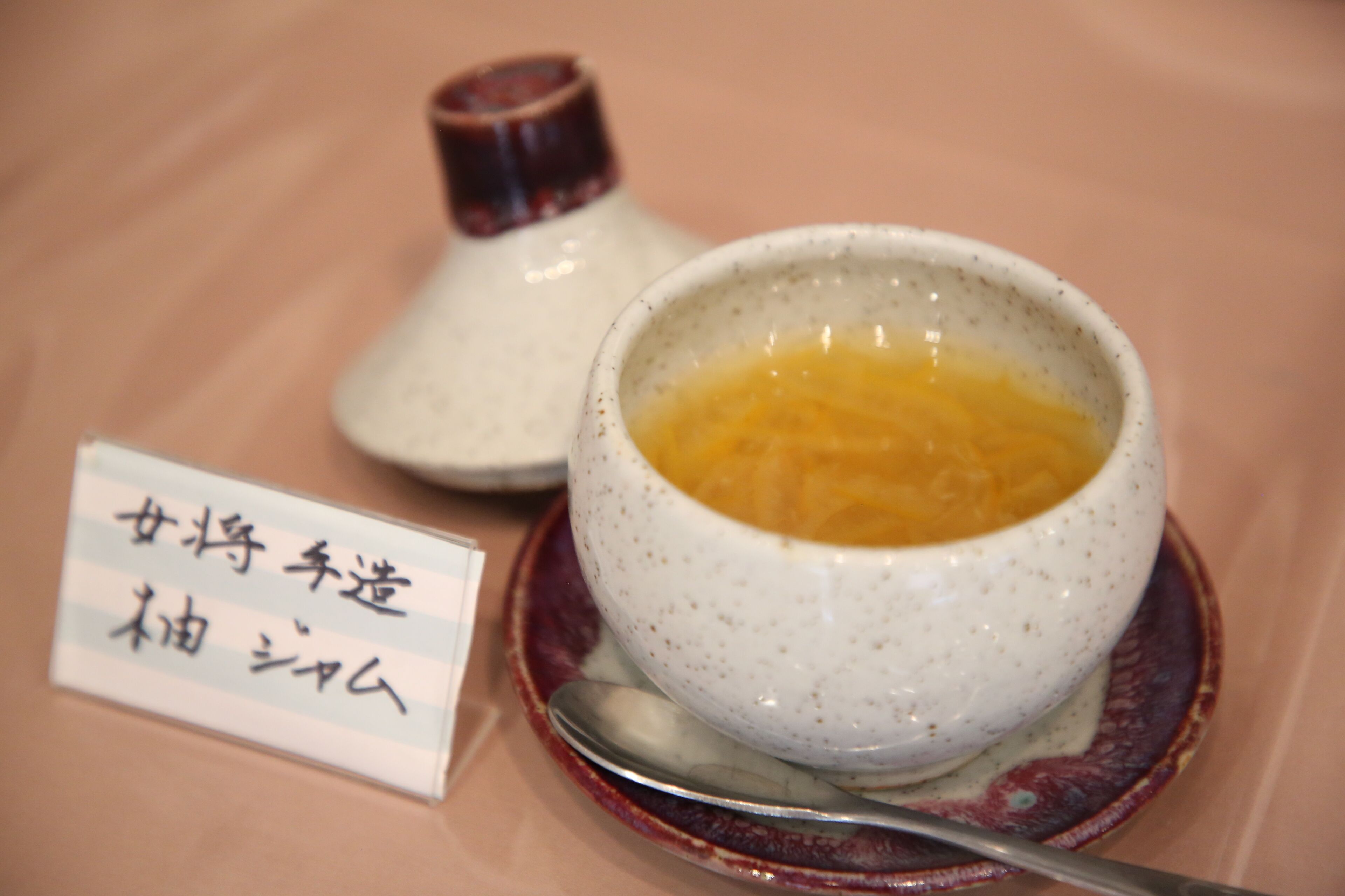 A bowl of soup with a spoon and a small dish with a label in front of it.