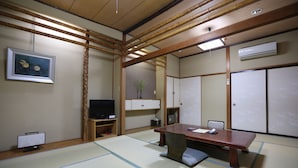 Une pièce de style japonais traditionnel, avec un sol recouvert de tatamis, une basse table en bois, un téléviseur et des portes coulissantes.