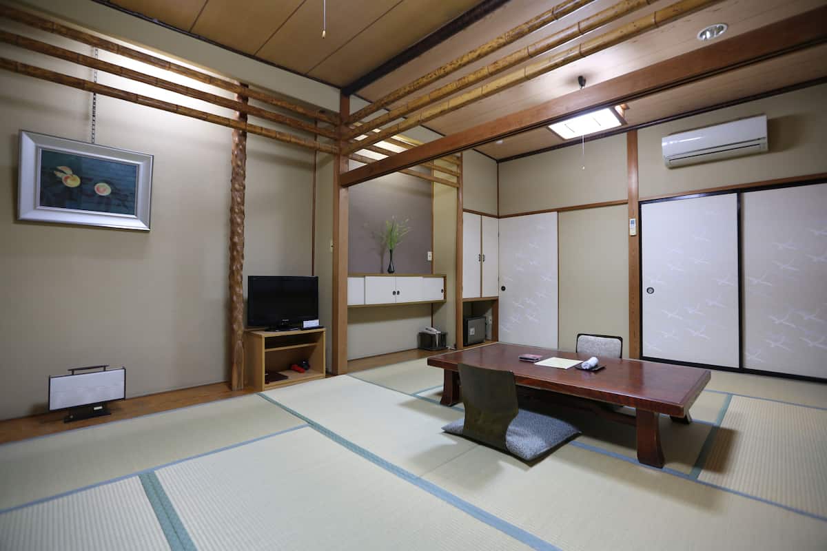 A traditional Japanese room with tatami flooring, a low wooden table, a television, and sliding doors.