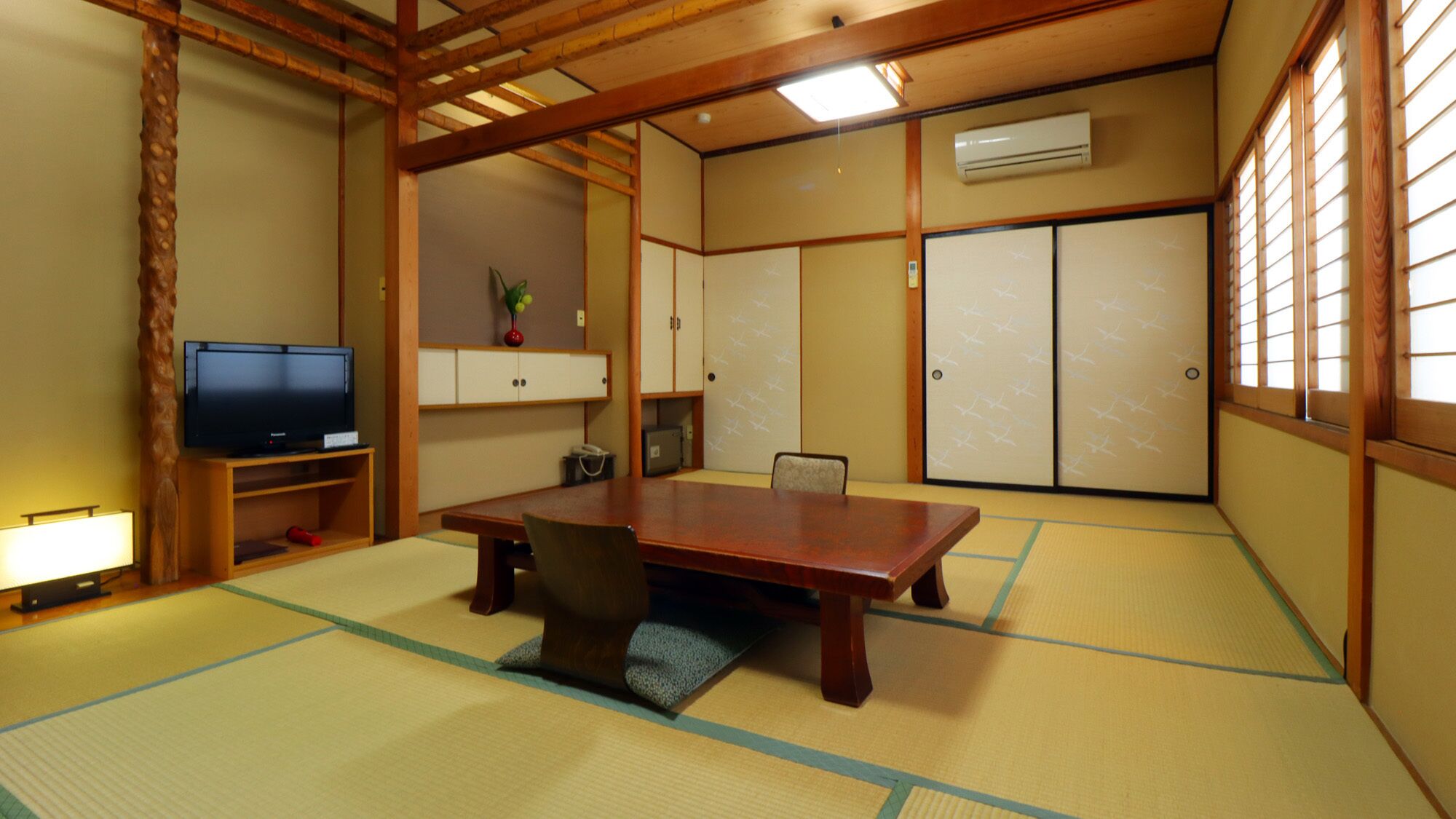 A traditional Japanese room with tatami flooring, a wooden table, a television, and sliding doors.