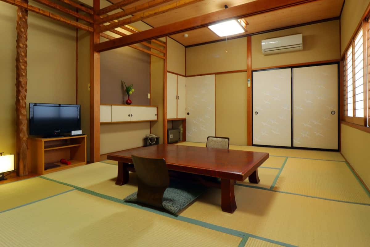 A traditional Japanese room with tatami flooring, a wooden table, a television, and sliding doors.