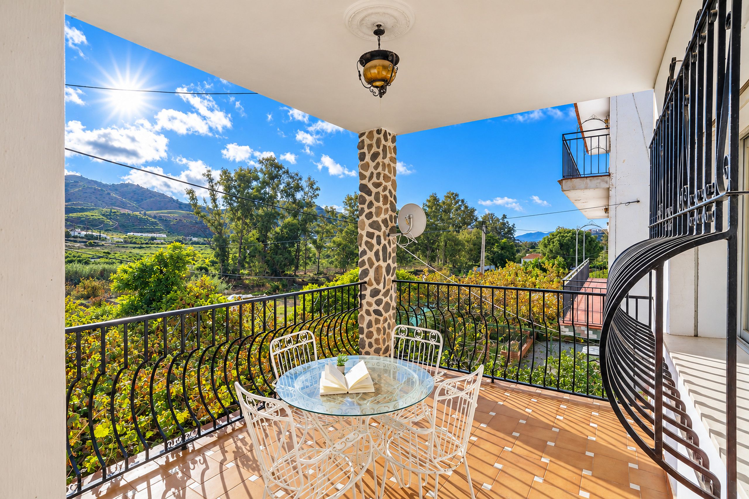 A balcony with a glass table and chairs, a giraffe sculpture, and a view of a mountainous landscape.