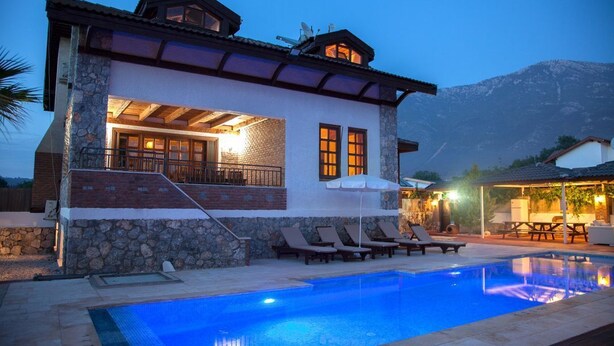 Une maison à deux étages avec une piscine, une façade en pierre et une vue sur les montagnes.