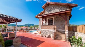 Une maison en pierre avec un balcon, une piscine et du mobilier d’extérieur.