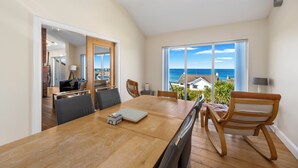 A dining area with a wooden table, chairs, and a view of the sea.