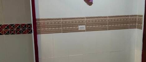 A bathroom with white tiled walls, a patterned tile border, a small purple flower decoration, and a colorful mat on the floor.