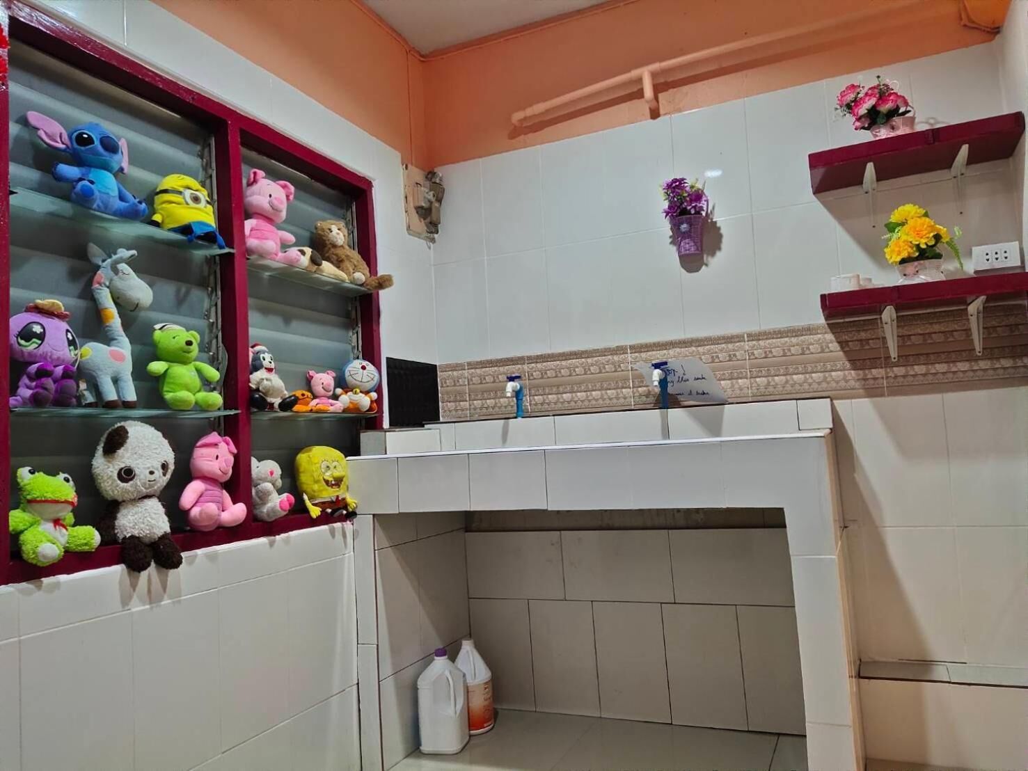 A bathroom with a shelf of plush toys, a tiled wall, a sink, and a toilet.