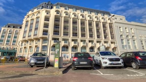 A multi-story building with a classic architectural style, featuring a central courtyard and a parking area with several cars.