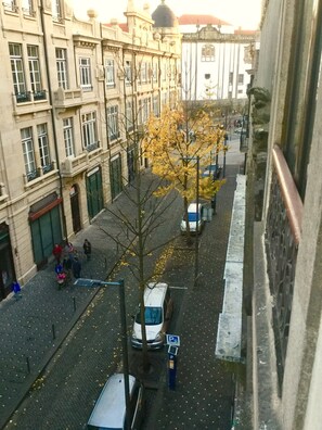 Straßenansicht mit parkenden Autos, einem Fußgänger und Gebäuden im klassischen Stil.