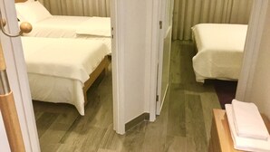 Habitación de hotel con dos camas, suelo de madera y una puerta que da a otra habitación.