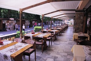 An outdoor café with wooden tables and chairs, covered by a white canopy. - Kamchia Park (Golden Sands)