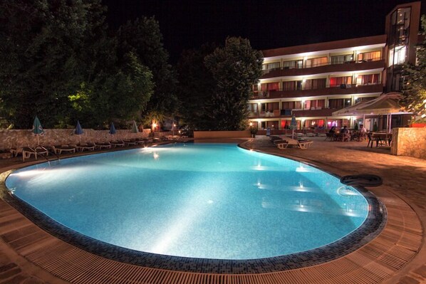 A swimming pool with lounge chairs and umbrellas, surrounded by a building with multiple balconies. - Kamchia Park (Golden Sands)