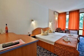 A hotel room with a wooden desk, a bed with floral bedspread, a chair, and a small table. - Kamchia Park (Golden Sands)