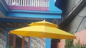 Un patio con una mesa redonda de madera y cuatro sillas, un paraguas amarillo y plantas en macetas.