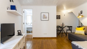 Ein modernes Wohnzimmer mit einem Flachbildfernseher, einer gelb gekissenen Couch und einem Essbereich mit Tisch und Stühlen.