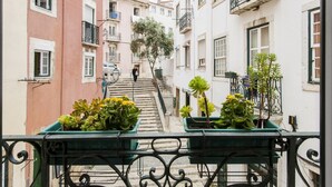 Eine schmale Straße mit Häusern an beiden Seiten, eine Person, die eine Treppe hinuntergeht, und Kübelpflanzen auf den Balkonen.