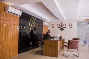 A modern office with a reception desk, a person working at the desk, and a sign that reads "Glee". - Glee Hotel (Lagos)