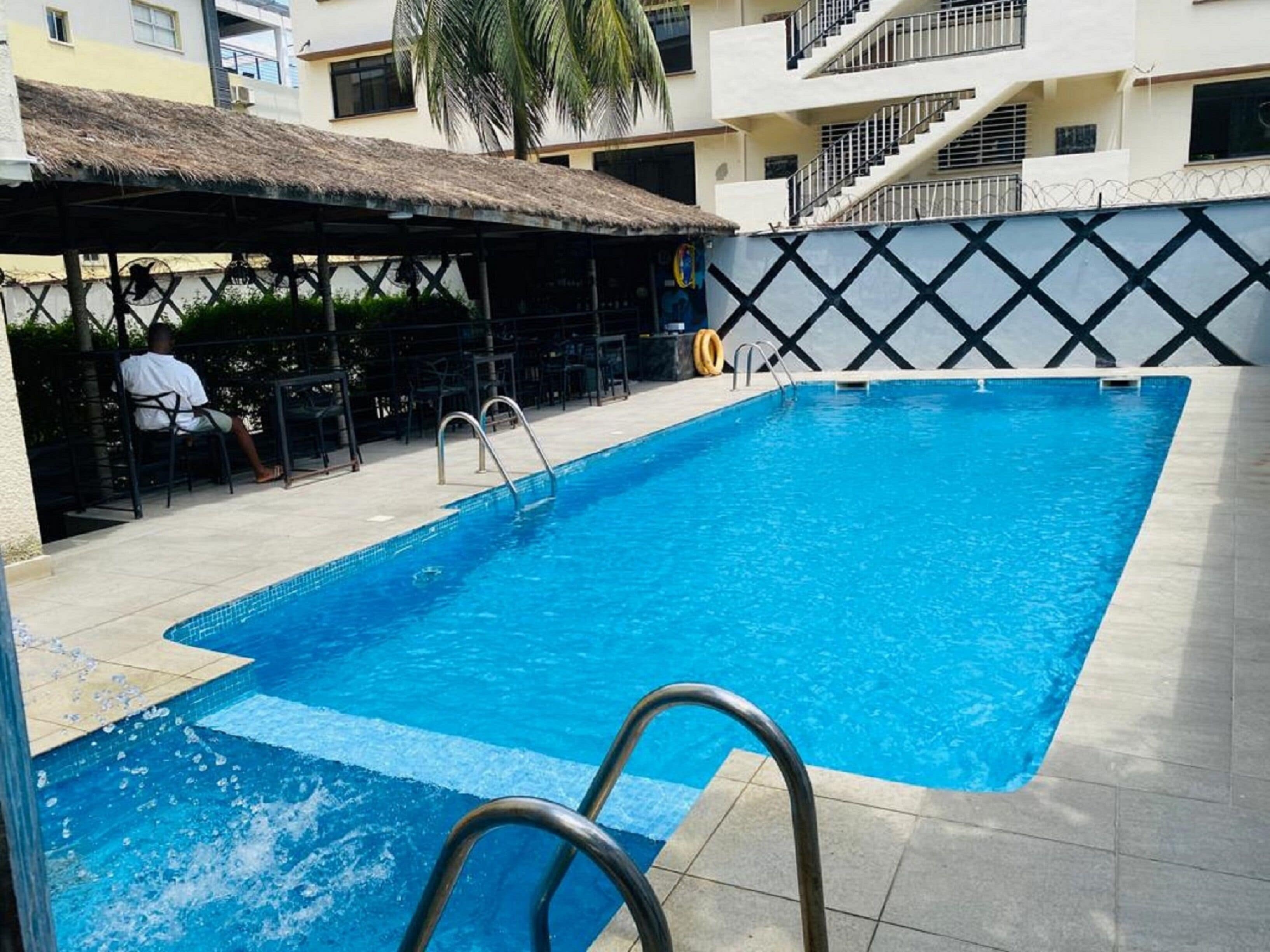 A swimming pool with a thatched roof seating area, a staircase, and a bar.