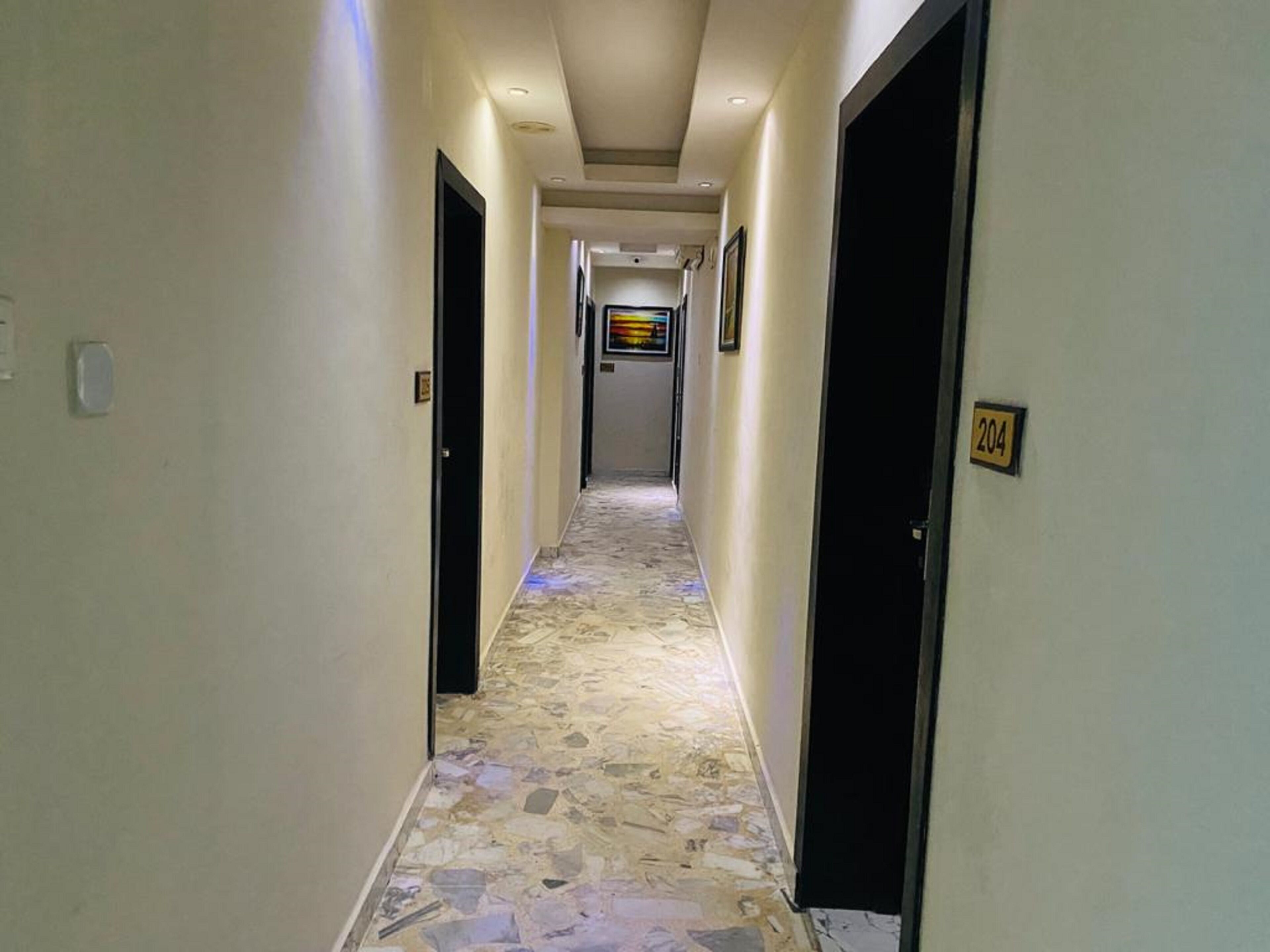 Un pasillo con suelo de piedra, puertas a ambos lados y un letrero con un número en la pared derecha.