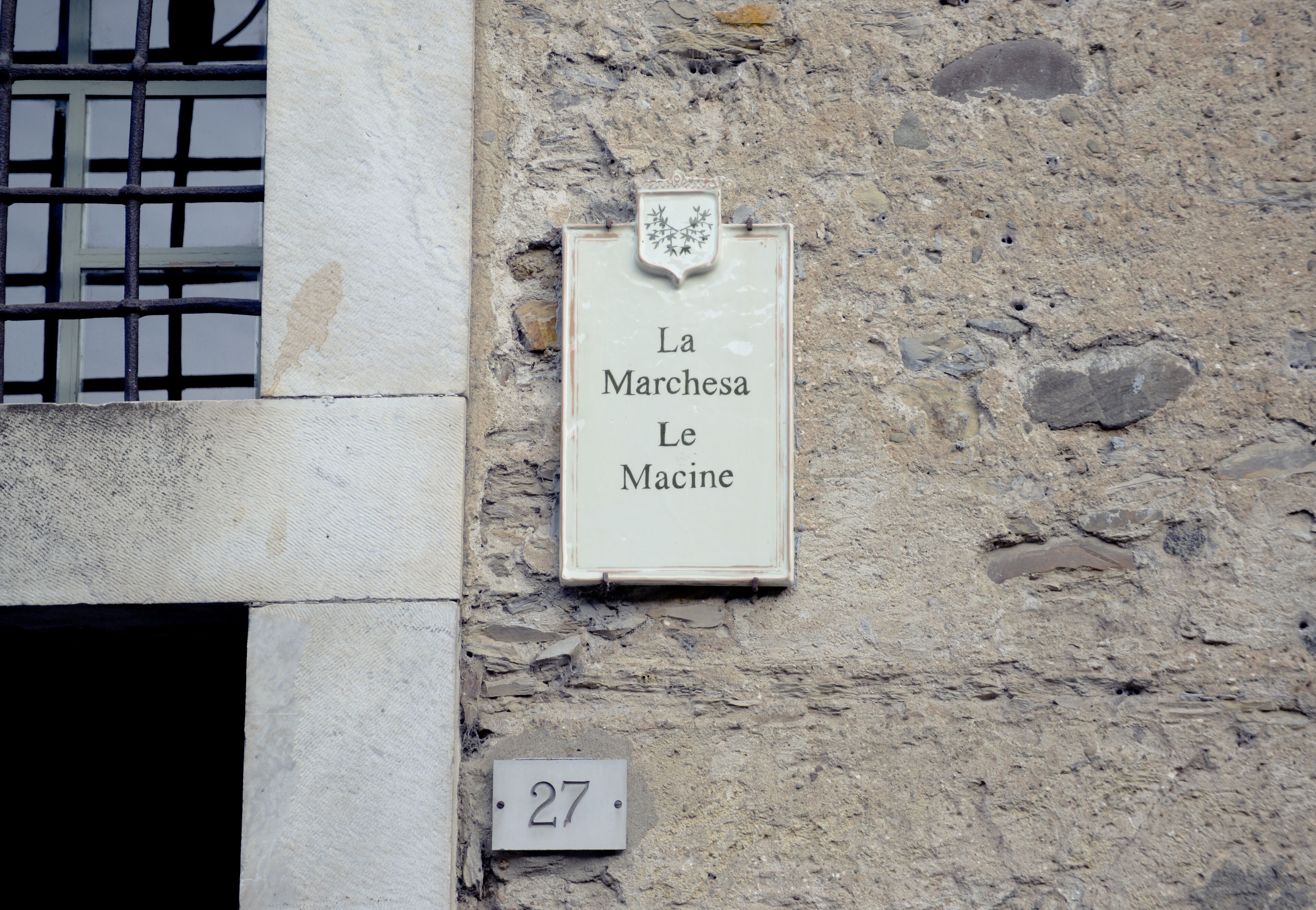 A building facade with a stone wall and a sign reading "La Marchesa Le Macine".