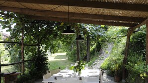 An outdoor dining area with a table set for four, surrounded by lush greenery and a wooden pergola overhead. - Ancient luxury oil mill (Ortonovo)