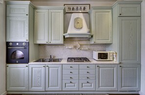 A kitchen with light green cabinetry, a stove, a microwave, and a clock on the wall.