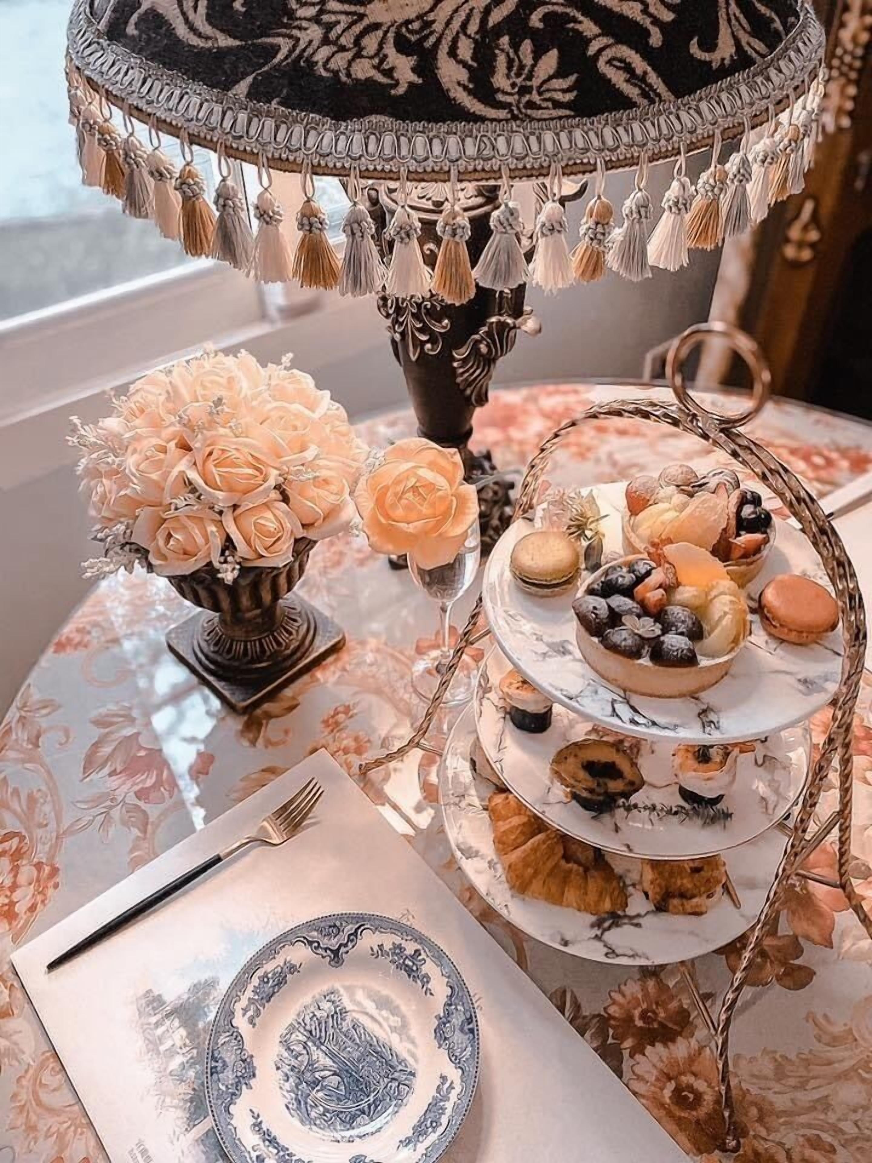 A table set with a vase of flowers, a tiered dessert stand, and a plate with a blue design.