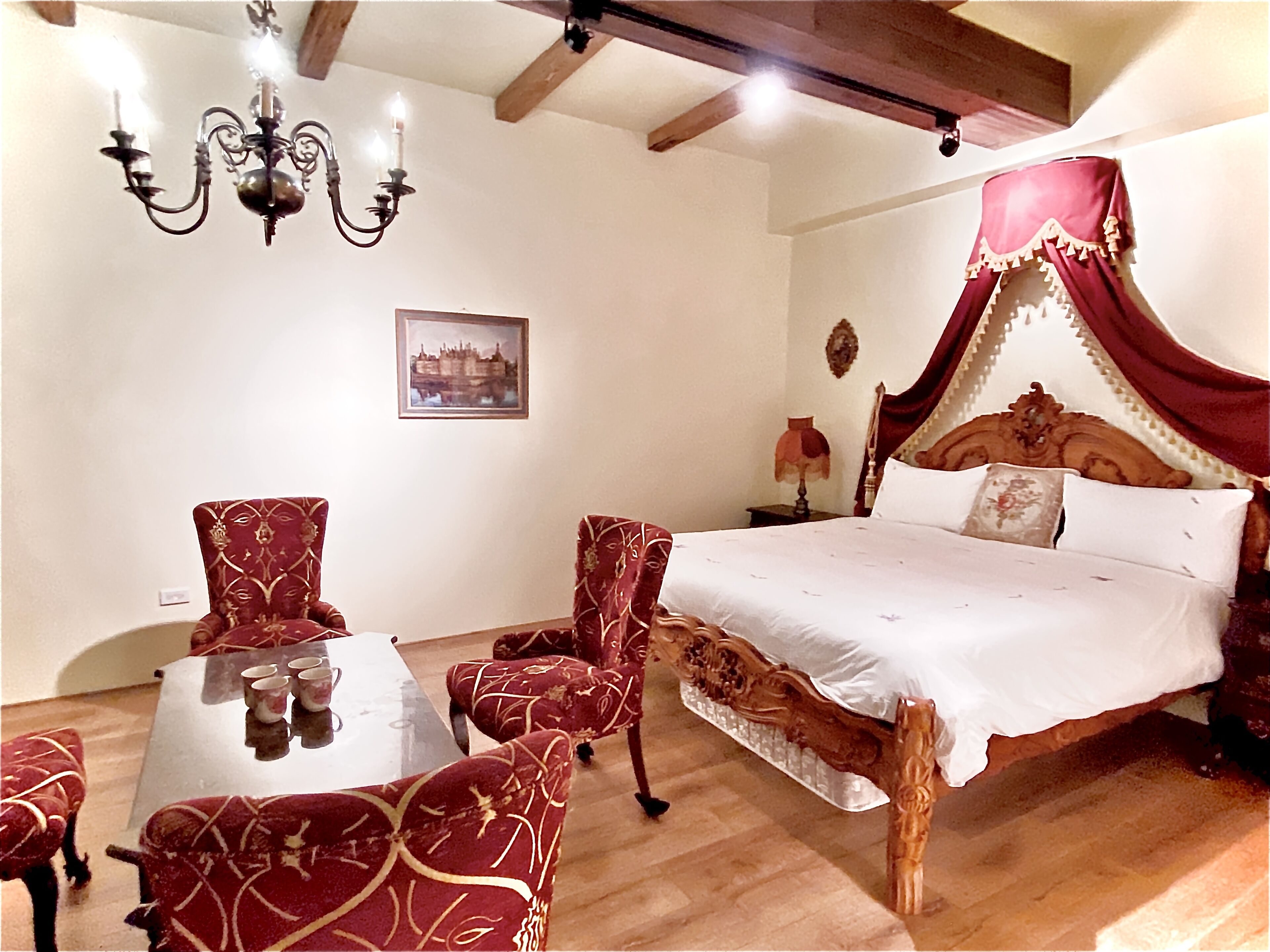 A bedroom with a four-poster bed, a chandelier, and a table with chairs.