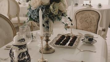 A dining table set with white tablecloth, silverware, a vase of flowers, and a cake.