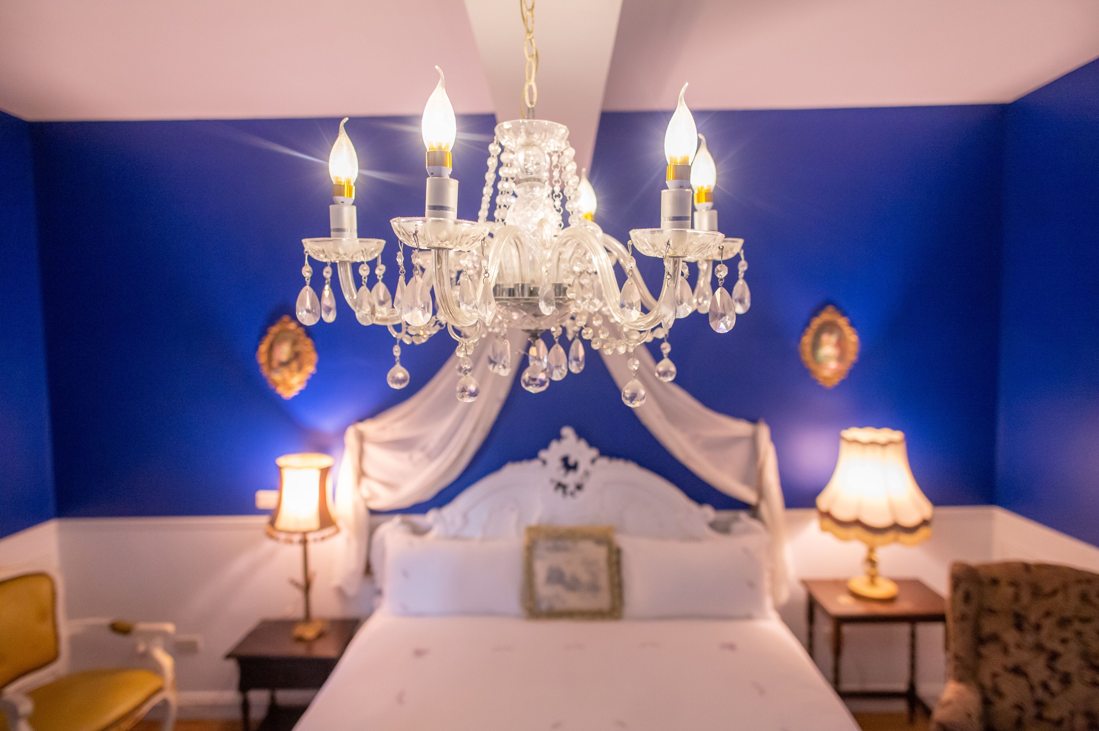 A bedroom with a chandelier, a bed, bedside tables, and a chair.