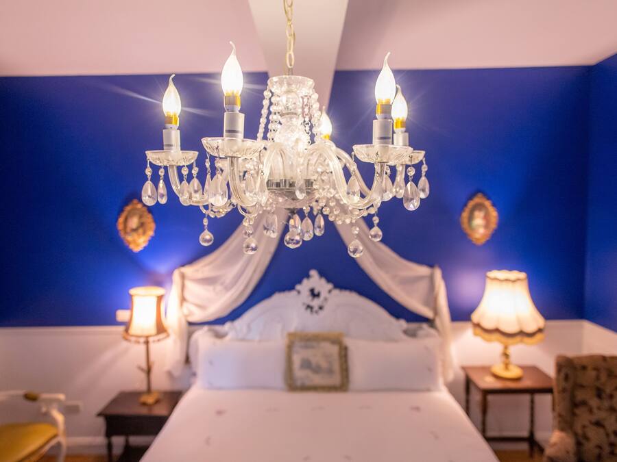 A bedroom with a chandelier, a bed, bedside tables, and a chair.