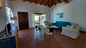 A spacious living area with a dining table, chairs, a sofa, and a TV on a stand.