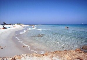 Una playa con agua cristalina, orilla arenosa y rocas al frente.