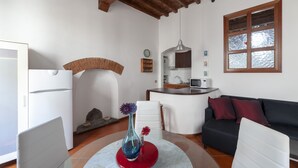 A modern living room with a white sofa, a red vase with flowers, a white chair, a kitchen area with a microwave, and a large window with a view of trees. - Independent 50 meters from the central and very Tuscan Duomo (Firenze)