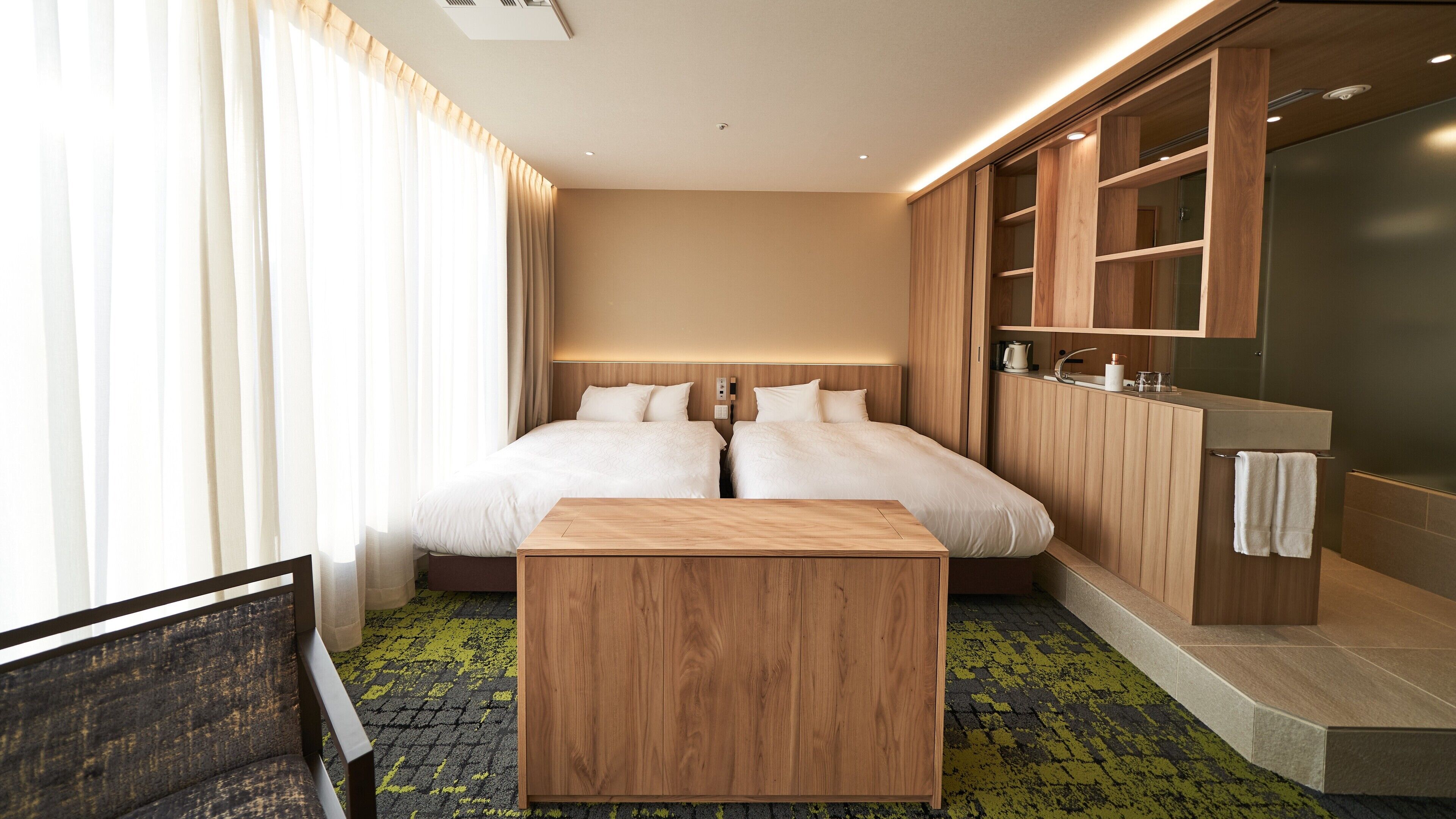 Habitación de hotel con una cama grande, una mesita de noche de madera, un armario empotrado y un baño con lavamanos y espejo.