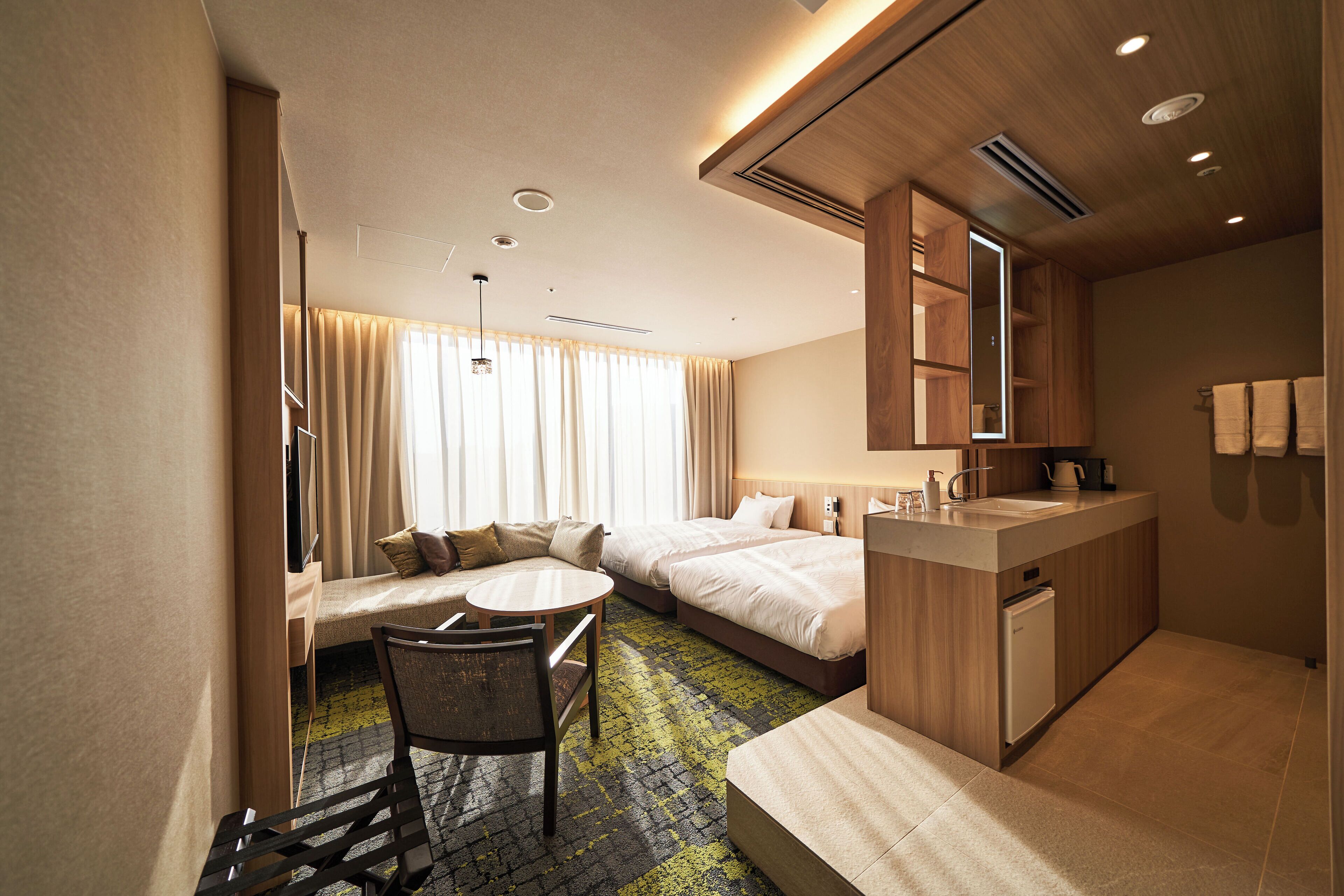 Habitación de hotel con sofá, dos camas individuales, una mesita, una silla, un lavabo y un espejo.