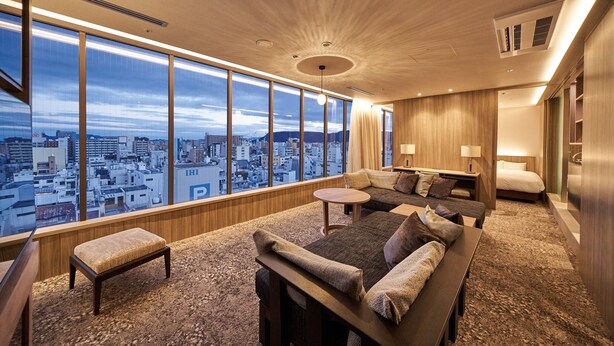 A modern hotel room with a large city view, a cozy seating area, and a separate bedroom. - WeBase TAKAMATSU - Hostel (Takamatsu)