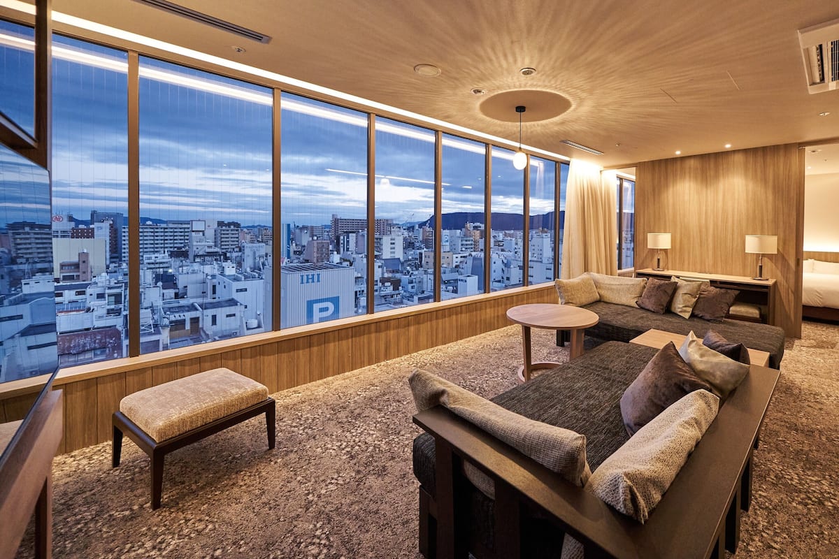 A modern hotel room with a large city view, a cozy seating area, and a separate bedroom.