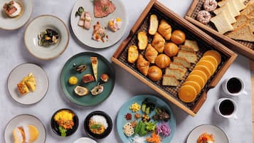 A variety of food items and pastries arranged on plates and a tray, with two cups of coffee nearby.