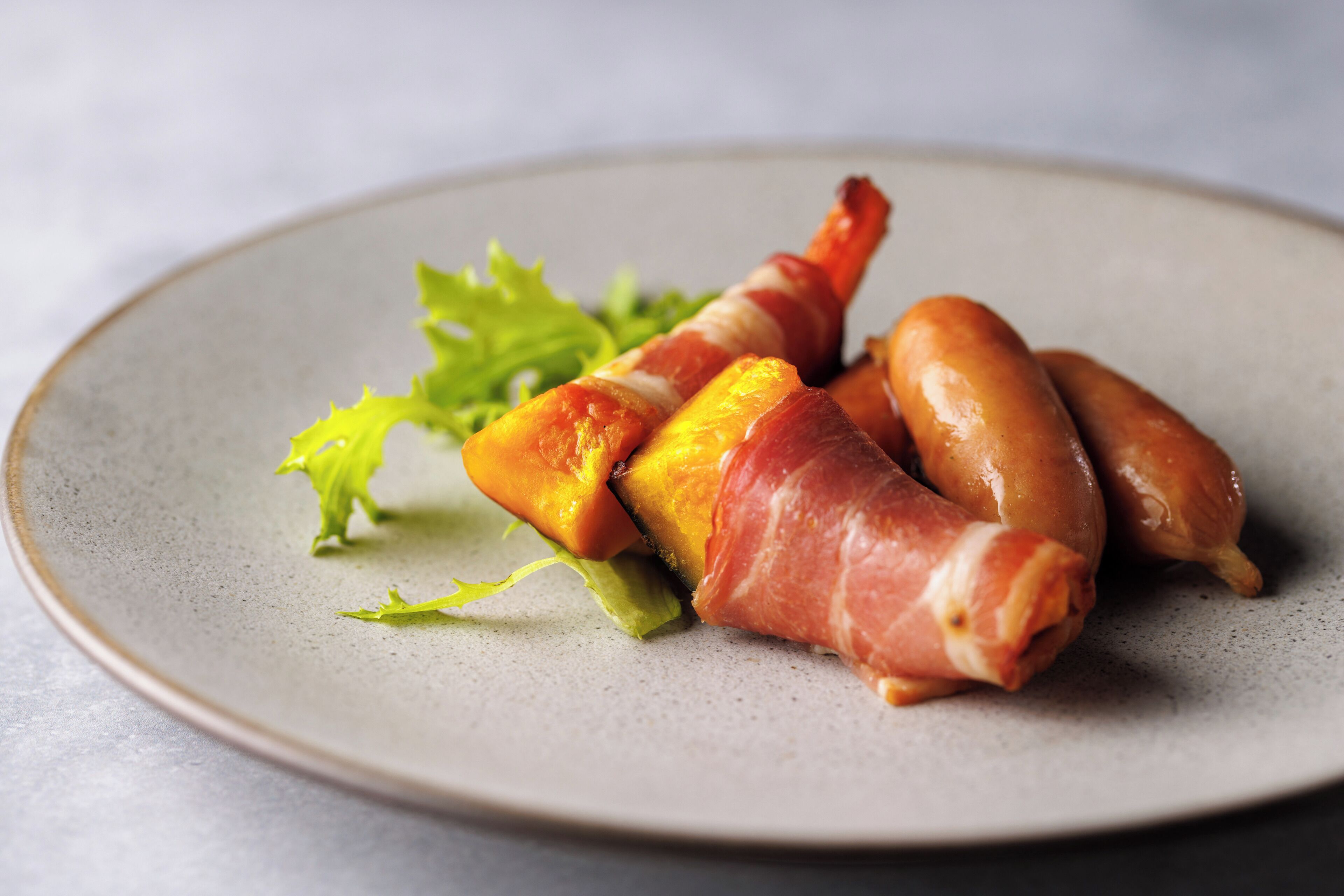 Une assiette en céramique, ornée d’une garniture verte, sur laquelle on trouve divers aliments, notamment un plat emballé et une saucisse.