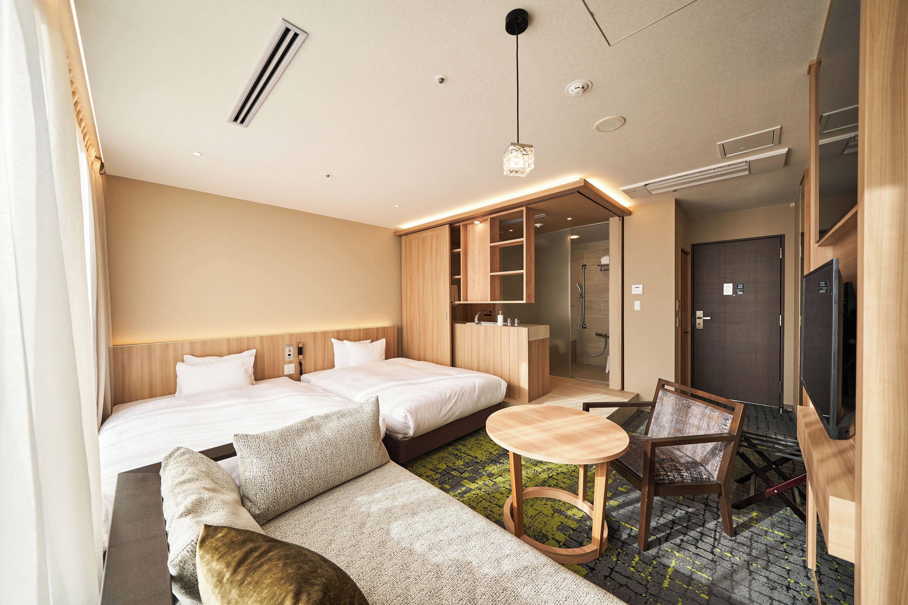 Ein Hotelzimmer mit zwei Betten, einem Sofa, einem kleinen Tisch, einem Fernseher und einem durch eine offene Tür einsehbaren Badezimmer.